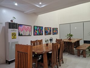 Ein Essbereich mit einem Holztisch und Stühlen, einer weißen Wand mit gerahmten Kunstwerken und einer Whiteboard.