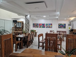A dining area with wooden tables and chairs, a stone pillar, and colorful artwork on the walls. - Reddoorz @ Jollydays Hotel Nueva Ecija (San Jose City)