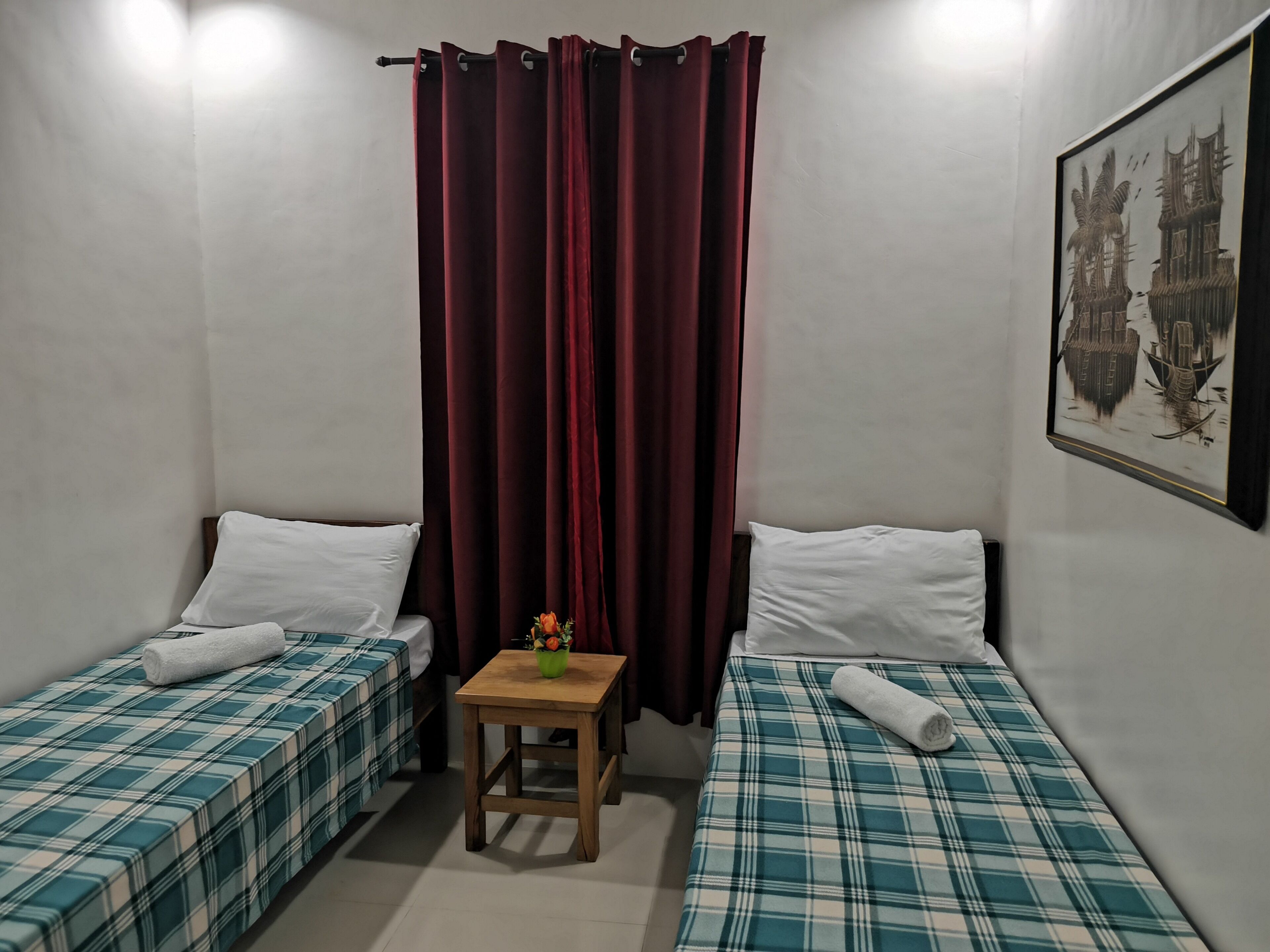 Une chambre avec deux lits, une petite table et un rideau.