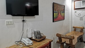 A room with a flat-screen TV mounted on the wall, a wooden table with a basket, a telephone, and a chair. - Reddoorz @ Jollydays Hotel Nueva Ecija (San Jose City)