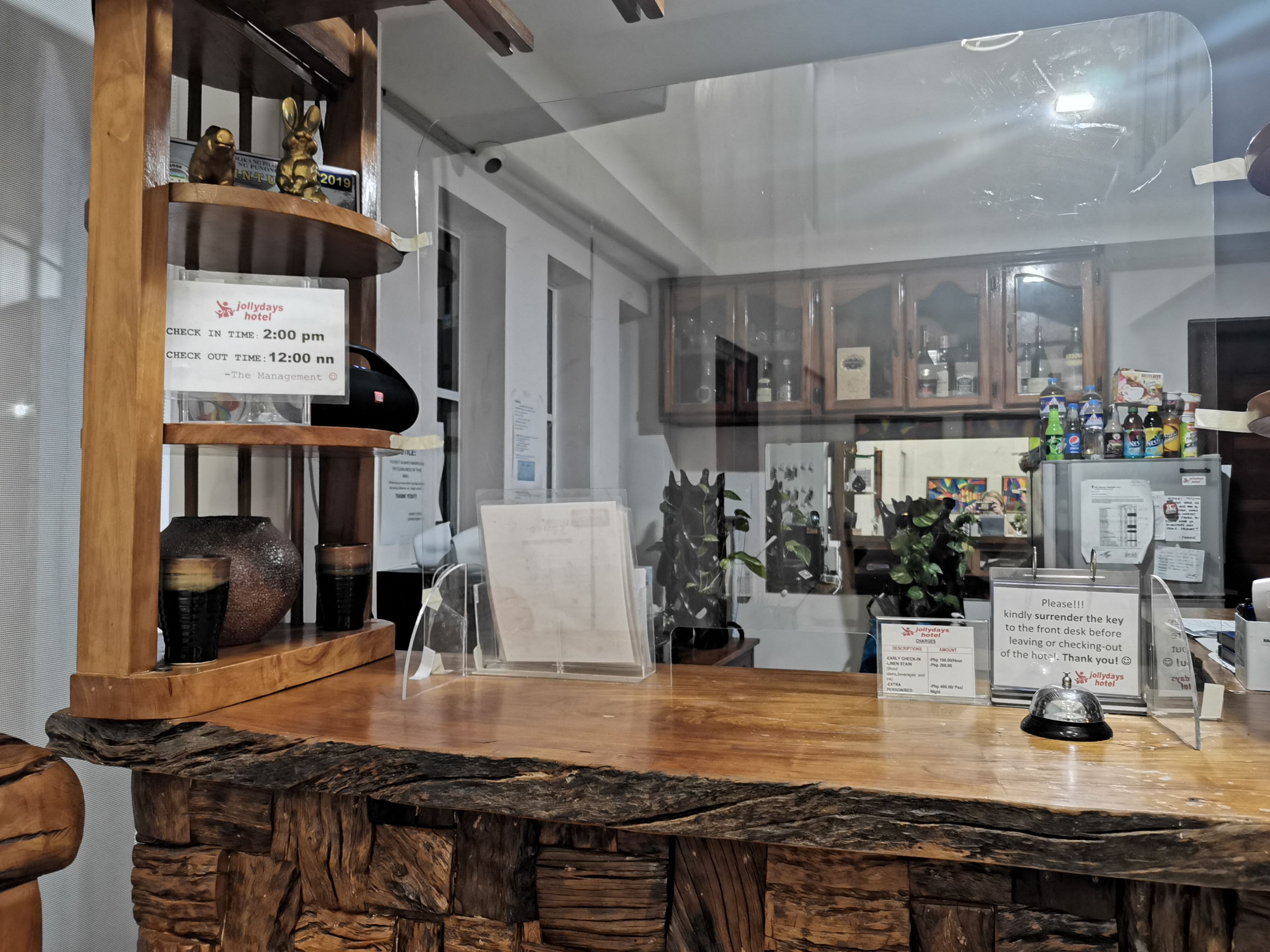 A hotel reception desk with a wooden counter, a glass display case, and a sign indicating check-in and check-out times.