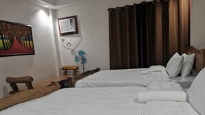 A hotel room with two beds, a wooden bench, a standing fan, and a painting on the wall. - Reddoorz @ Jollydays Hotel Nueva Ecija (San Jose City)