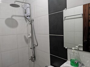Un baño con ducha, lavamanos con dispensador de jabón y espejo.