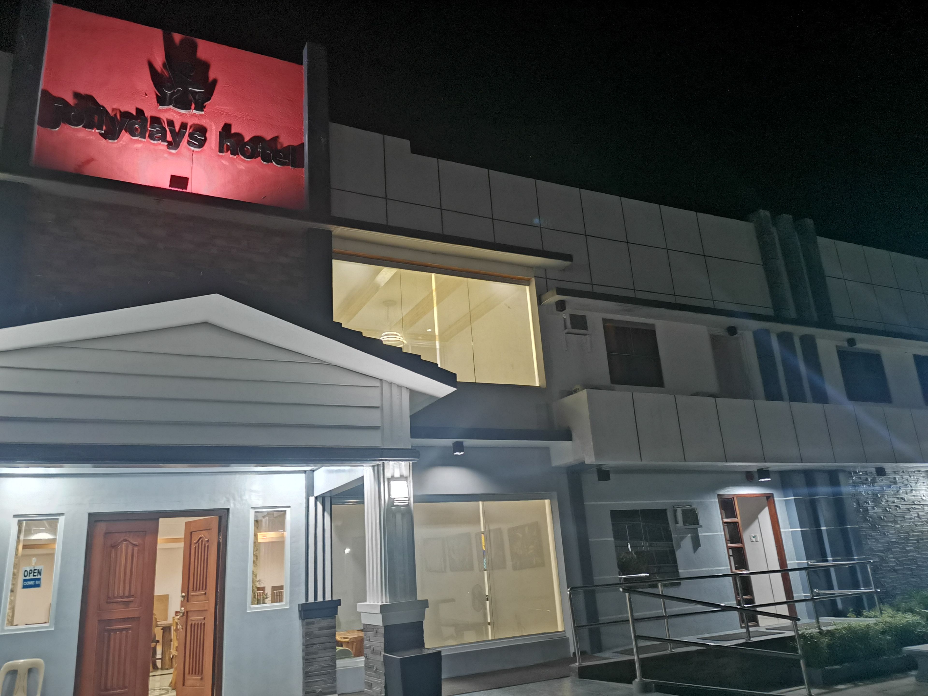 A hotel with a prominent red sign, a glass entrance, and a staircase leading to the entrance.