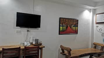 A dining area with a table and chairs, a flat-screen TV mounted on the wall, and a framed painting above the table.
