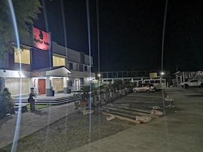 A hotel with a modern facade, a visible entrance, and a parking area with several vehicles. - Reddoorz @ Jollydays Hotel Nueva Ecija (San Jose City)