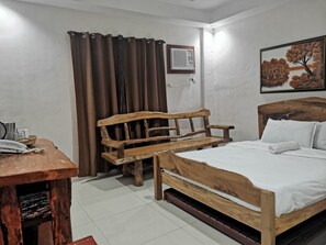 Ein Zimmer mit einem hölzernen Bett, einer Holzbank, einem kleinen Tisch mit Telefon und einem Bild an der Wand.
