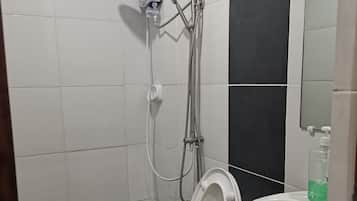 Une salle de bain avec des toilettes blanches, une douche équipée d’un pommeau de douche amovible et un lavabo avec un distributeur de savon.