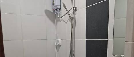 A bathroom with a white toilet, a shower with a handheld showerhead, and a sink with a soap dispenser.