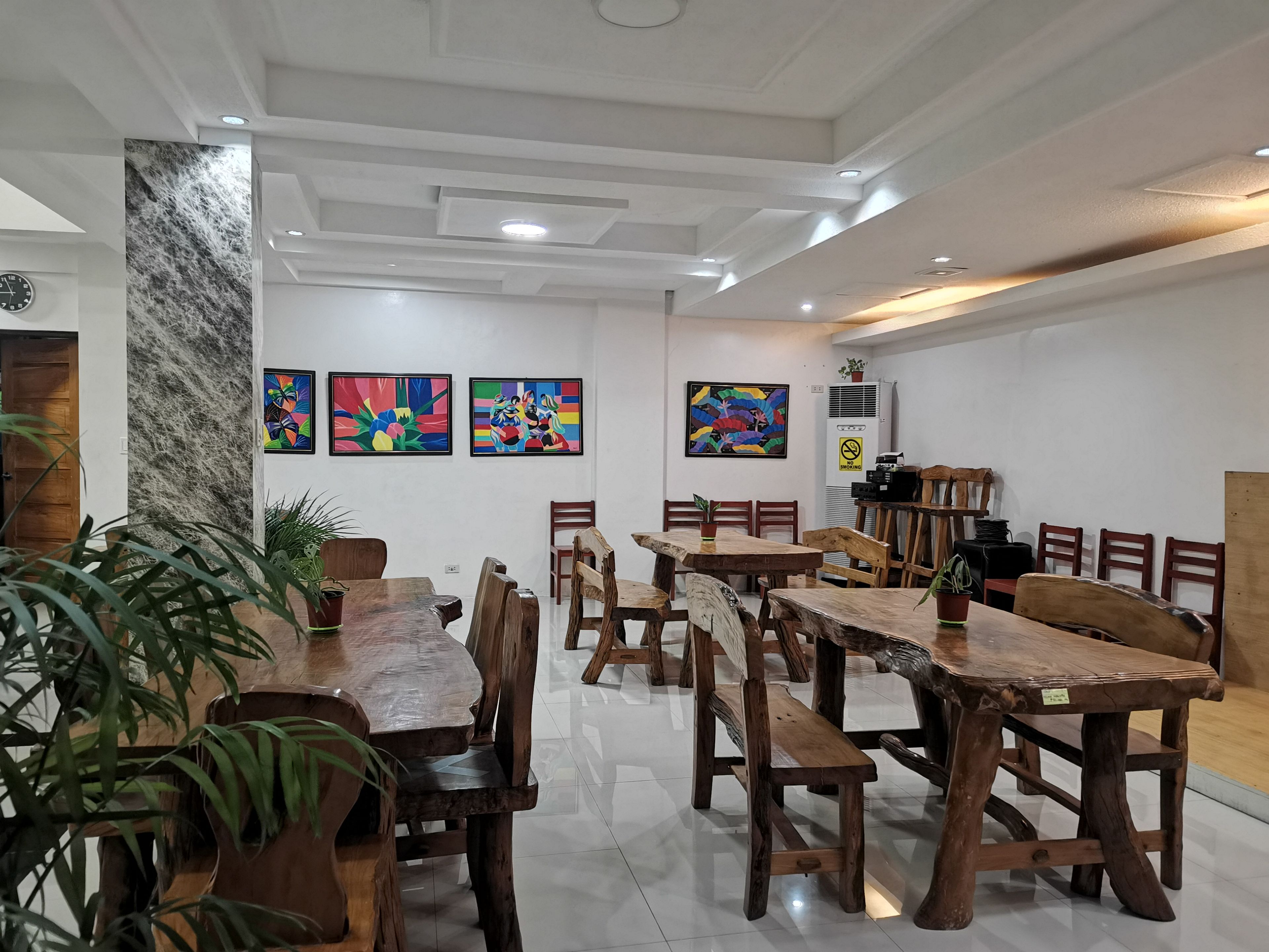 A dining area with wooden tables and chairs, white walls, and colorful artwork.