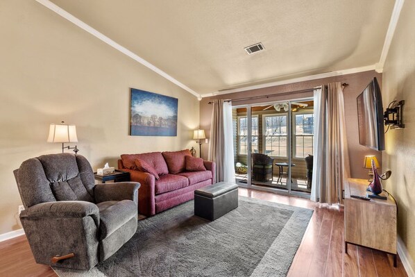 A living room with a sofa, armchair, ottoman, and a large window with curtains.