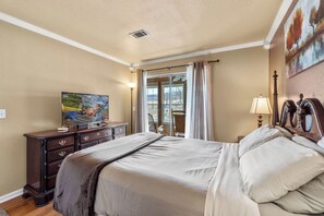 A hotel room with a bed, a dresser, a television, a window with curtains, and a painting on the wall.