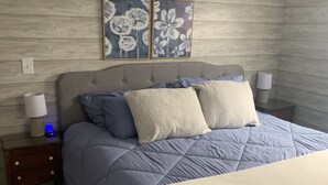 Ein Schlafzimmer mit einem Bett, einem Nachttisch, einer Lampe und zwei Blumenbildern an der Wand.