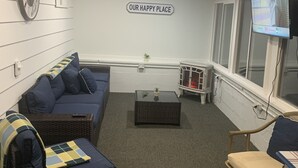 Ein gemütliches Zimmer mit einem blauen Sofa, einem Korbstuhl, einem kleinen Tisch und einem an der Wand befestigten Fernseher.