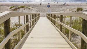 A wooden boardwalk leading to a beach with a clear view of the ocean.