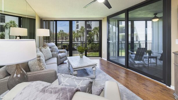 A spacious living room with a ceiling fan, a large window, and a balcony with outdoor furniture.