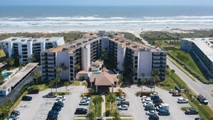 A multi-story hotel with a parking lot in front, located near a beach with ocean views.