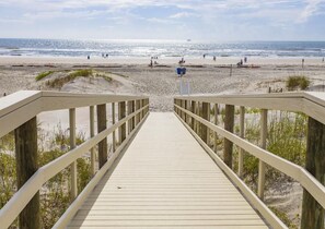 A wooden boardwalk leading to a beach with a clear view of the ocean.