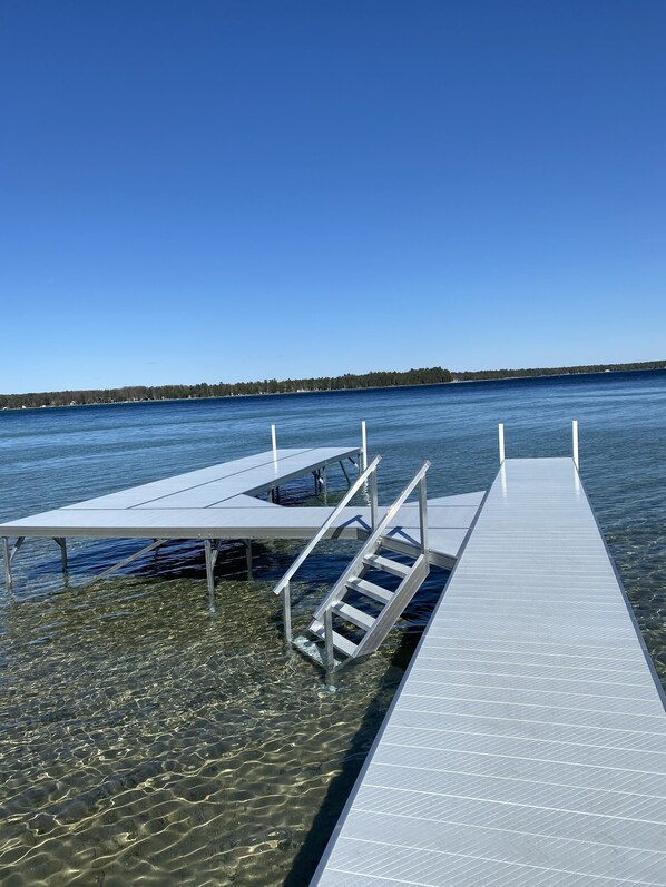 A clear view of a dock extending into calm water with a distant shoreline. - BEAUTIFUL LAKE FRONT NEWLY RENOVATED COTTAGE 2021 (Roscommon)