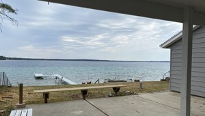 Eine Terrassensitzgruppe am Seeufer mit Betonboden, einer Holzbank und einem kleinen Steg, der ins Wasser führt.