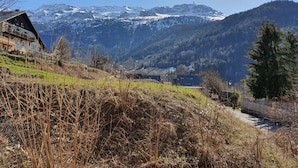 Eine Berglandschaft mit schneebedeckten Gipfeln, einem Gebäude mit Balkonen und einem bewaldeten Hügel.