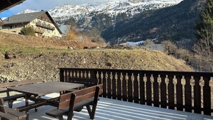 Eine Holzterrasse mit Picknicktischen und Bänken mit Blick auf eine gebirgige Landschaft mit schneebedeckten Gipfeln und einem Fluss.