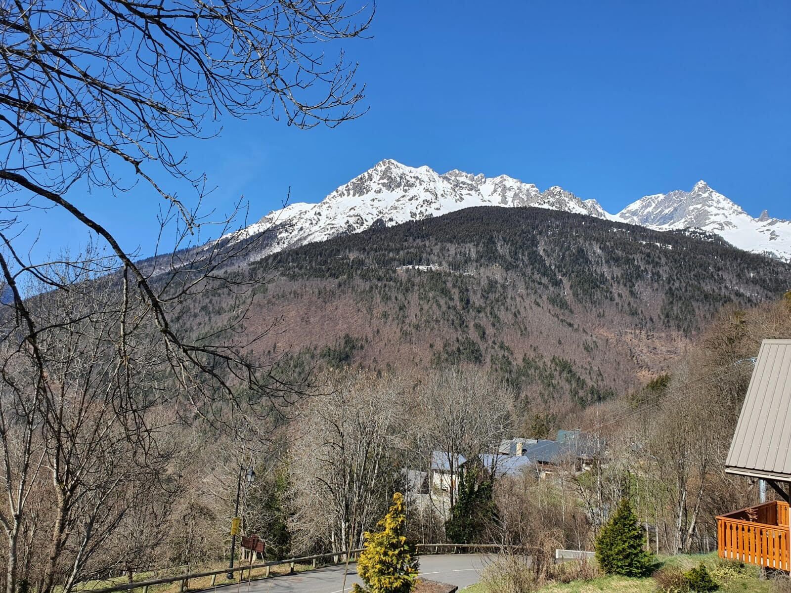A mountain landscape with snow-capped peaks, a road, and a building with a wooden deck.