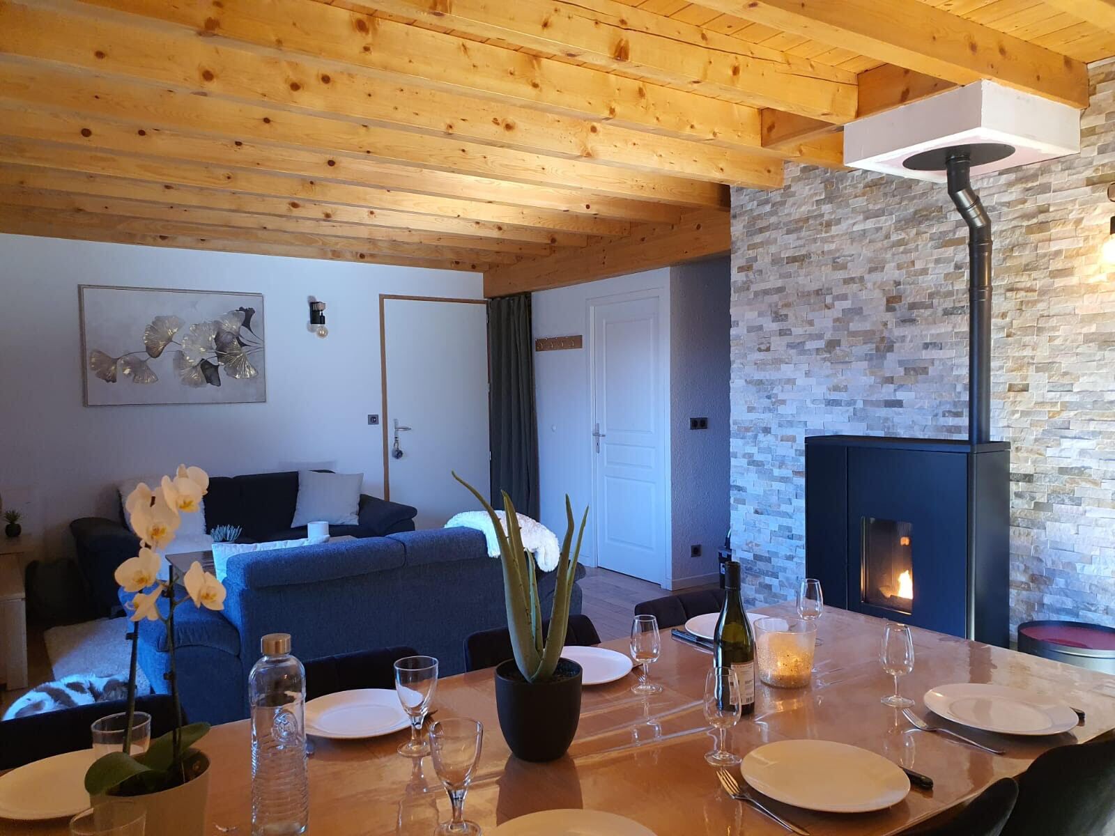 Un salon chaleureux avec une cheminée, un plafond en bois et un coin repas aménagé pour prendre un repas.