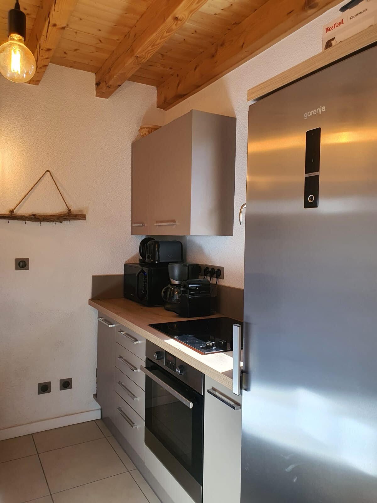 A compact kitchen with a built-in oven, a coffee maker, and a stainless steel refrigerator.