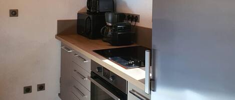 A compact kitchen with a built-in oven, a coffee maker, and a stainless steel refrigerator.