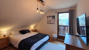 Ein Schlafzimmer mit einem Bett, Nachttischlampen, einem Schreibtisch mit Fernseher und einem Fenster mit Vorhängen.
