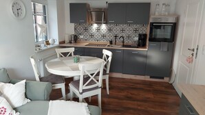 Une cuisine compacte avec un coin repas, comprenant une table ronde, des chaises, un four encastré et un four à micro-ondes.
