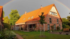 Une maison à deux étages avec un toit rouge, une véranda et une façade en briques.