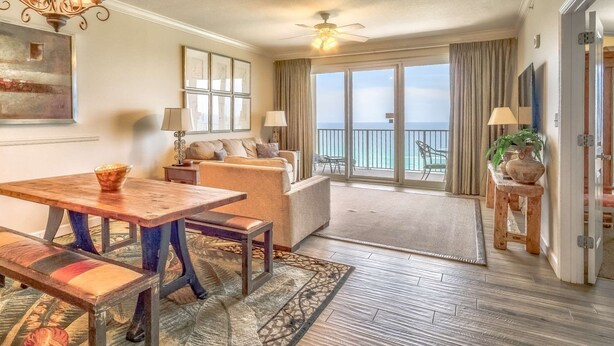 A spacious living room with a wooden dining table, sofas, and a balcony with a view of the ocean. - Grandview East 903 (Panama City Beach)