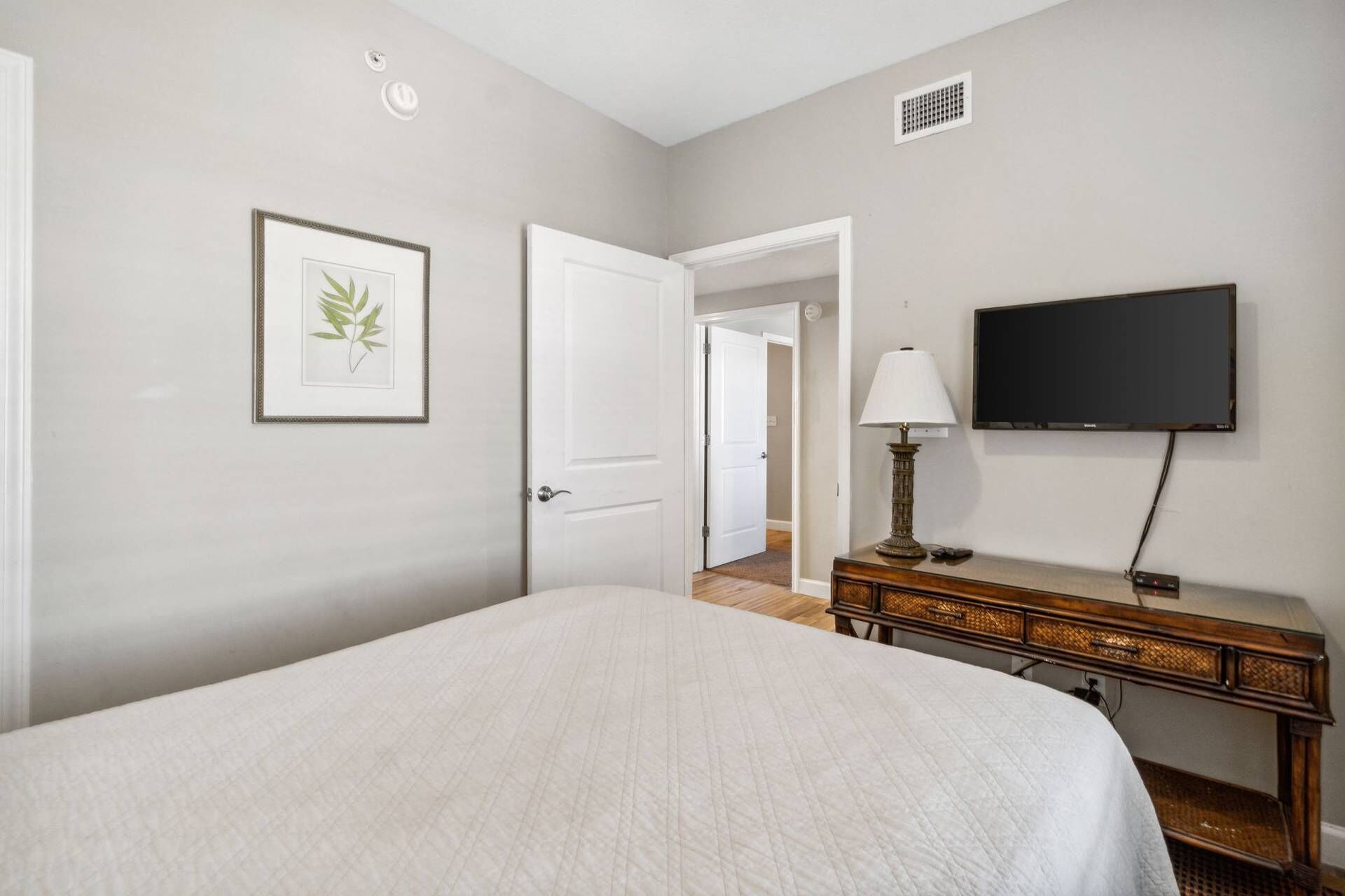 A bedroom with a bed, a dresser, a television, and a door leading to another room.
