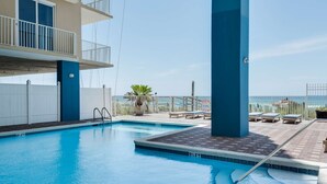 A swimming pool with a view of the ocean, a balcony with a railing, and lounge chairs. - Grandview East 903 (Panama City Beach)