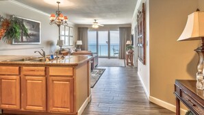 A spacious kitchen with a central island, a dining area with a view, and a hallway leading to a balcony. - Grandview East 903 (Panama City Beach)