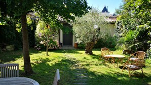 Un jardín con un banco de madera, una mesa redonda y sillas de mimbre.