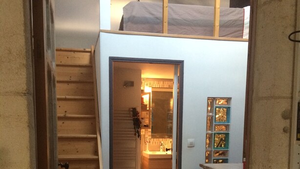 Una escalera conduce a un dormitorio superior con una cama nido, un baño pequeño y suelo de madera.