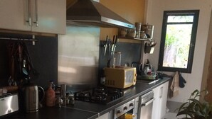 Cocina moderna con armarios blancos, encimera negra y electrodomésticos de acero inoxidable. Hay una ventana que proporciona luz natural y vistas a la vegetación exterior.