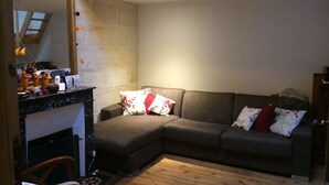 Una sala de estar con un sofá seccional, piso de madera, una chimenea y un espejo que refleja parte del espacio.