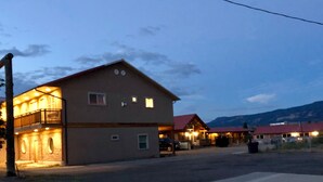 A two-story building with a balcony on the ground floor, a small attached garage, and a mountain backdrop. - Beautiful Studio Suite (Loa)