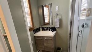 A bathroom with a shower, a sink with a mirror, and a window. - Beautiful Studio Suite (Loa)