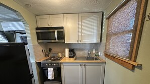 A compact kitchen with white cabinets, a stainless steel stove, a microwave, and a sink. - Beautiful Studio Suite (Loa)