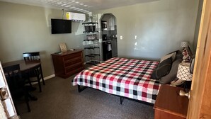 A compact bedroom with a bed, a desk, a dresser, a kitchenette, and a television. - Beautiful Studio Suite (Loa)