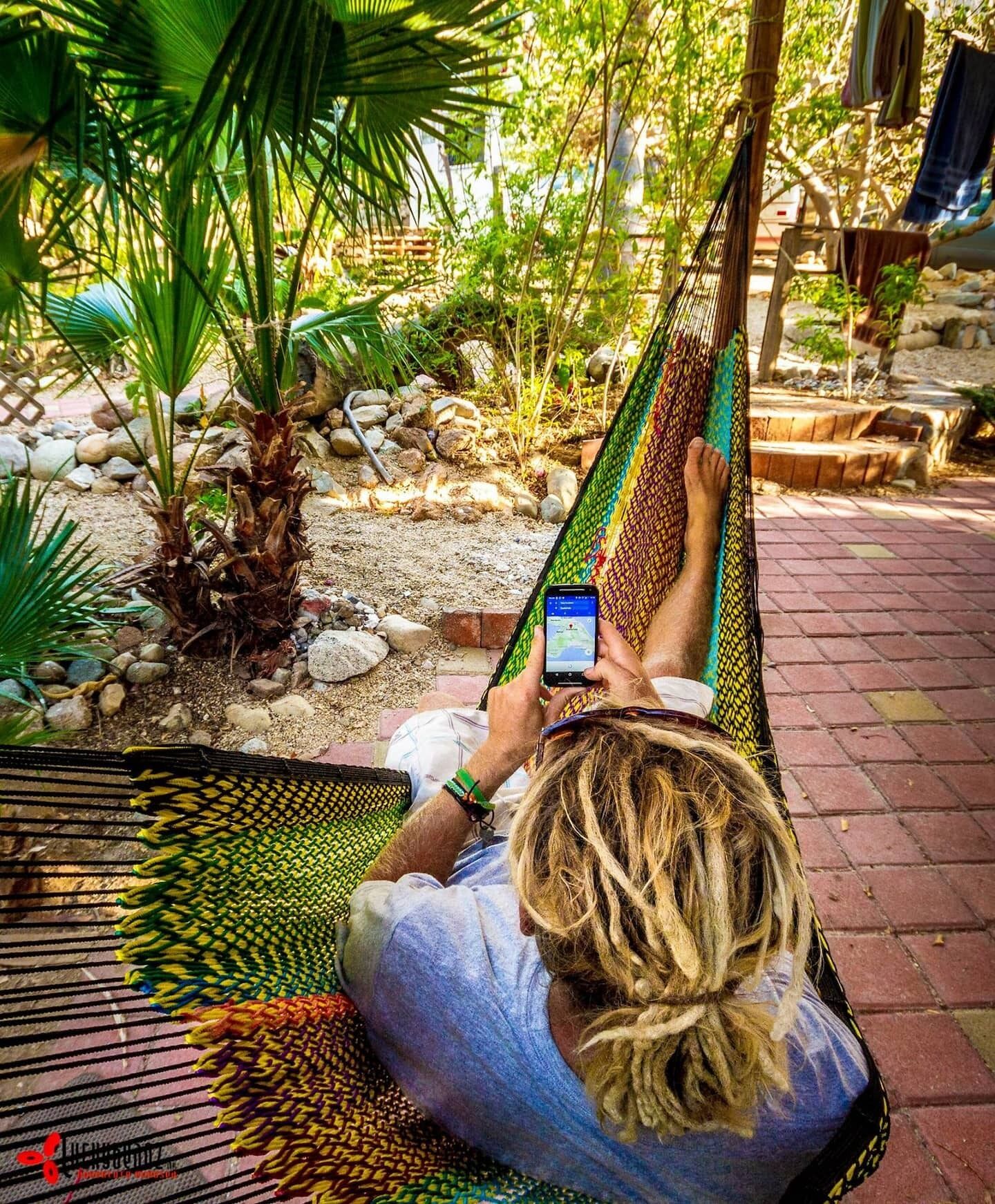 Uma pessoa relaxando em uma rede em um jardim com pedras e plantas.
