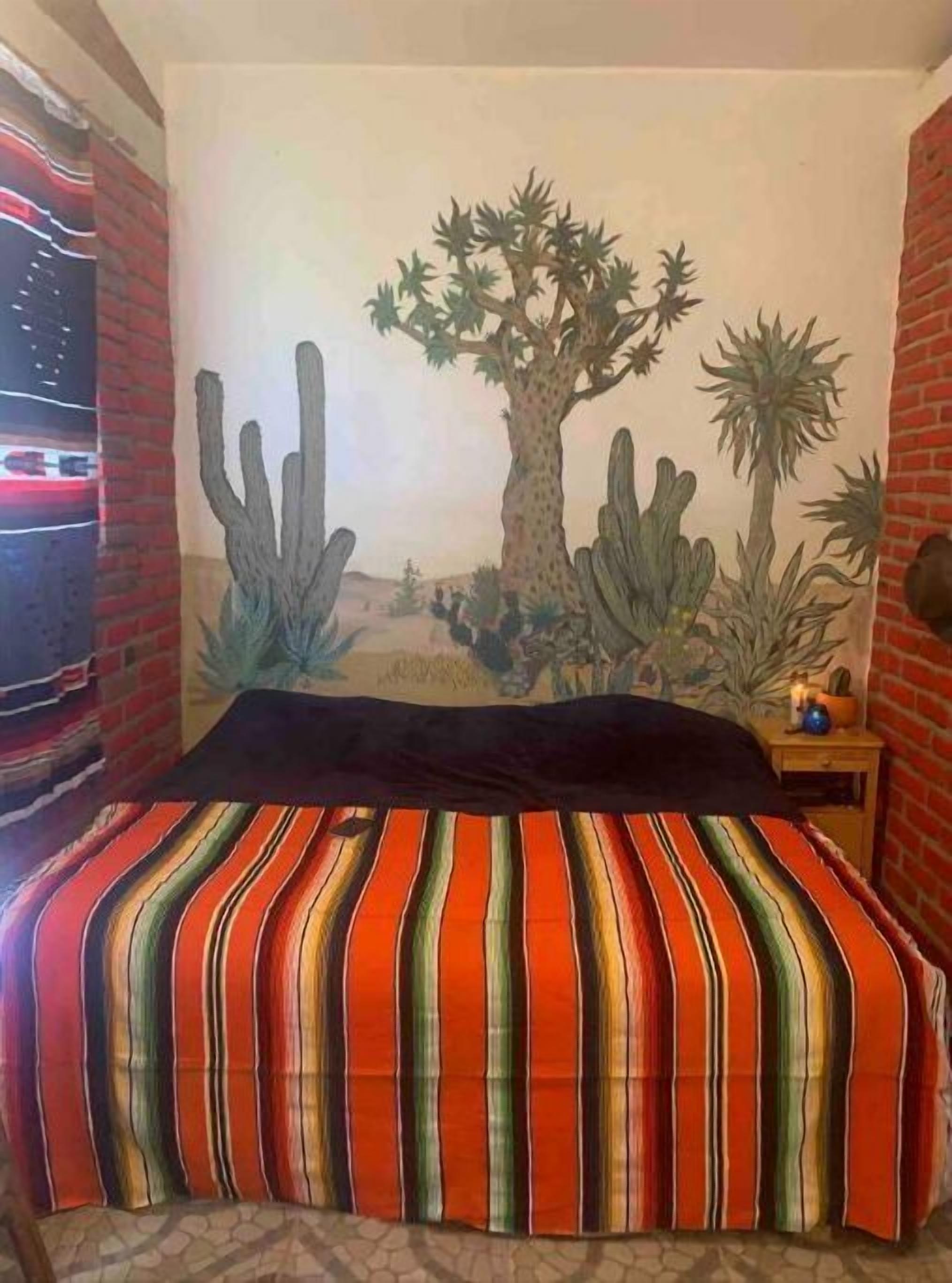 A bedroom with a mural of desert cacti and a bed with a striped bedspread.