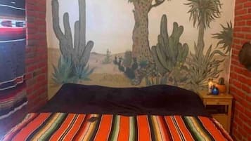 A bedroom with a mural of desert cacti and a bed with a striped bedspread.