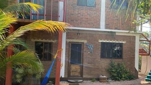 A two-story brick building with a front door, windows, and a small garden area with a hammock and palm trees.