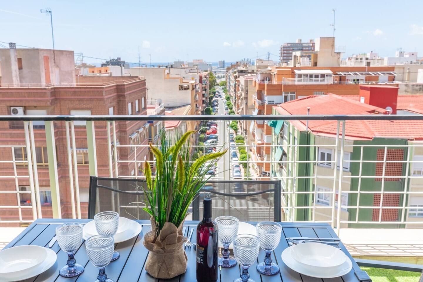 A balcony with a table set for dining, overlooking a cityscape with buildings and a clear sky.